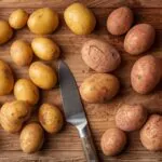 different varieties of potatoes including Russet and Yukon Gold arranged on wooden cutting board with kitchen knife for mashed potato preparation